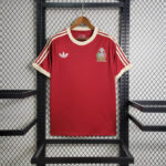 Red Adidas soccer jersey on a hanger with cream collar and stripes, featuring a white trefoil logo and a Mexican crest on the chest.