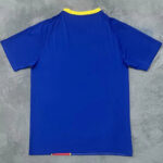 Back view of a royal blue T-shirt with a yellow collar trim on a gray surface, small color accent at the bottom hem.