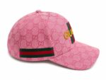 Pink Gucci baseball cap with an all-over GG monogram, featuring a green-red-green strap and a yellow Gucci logo on the front.