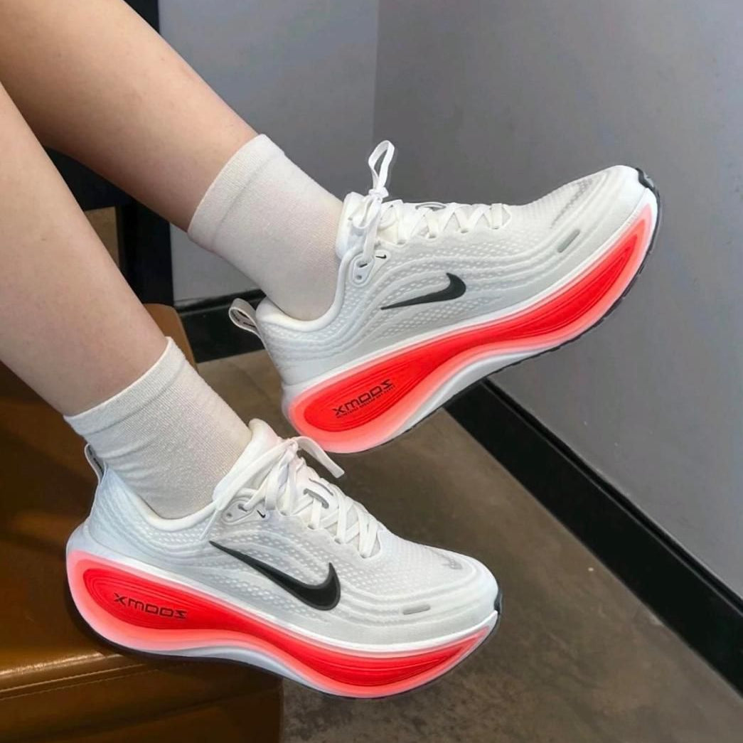 6e576e23-4224-4614-9b9d-84f67d7f3aee White Nike running shoes with black swoosh and bright red glowing midsole, worn with white socks by a person seated on a bench.