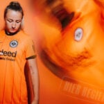 6eOuwbL7TZWhiAS | UAE SPORT STORE Young woman in a bright orange sports jersey looks down, with a blurred teammate in motion to the right.