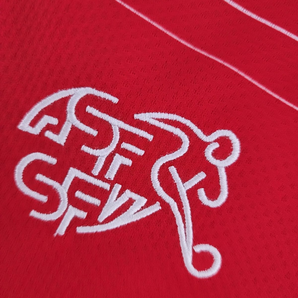 Close-up of red textile with white embroidered cursive lettering, cropped.