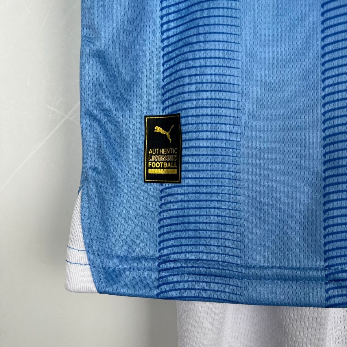 Close-up of blue jersey fabric with a black tag reading 'AUTHENTIC LICENSED FOOTBALL' and a yellow Puma logo.