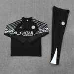 Black athletic tracksuit with white wing stripe design across the chest and sleeves, features Paris Saint-Germain crest and Qatar Airways logo on the jacket.