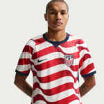 Man wearing a USA soccer jersey with red wavy stripes and a navy collar, facing the camera.