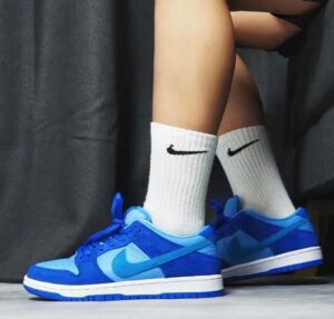 Blue Nike sneakers with white crew socks, shown from the side as a person stands indoors on a light floor.