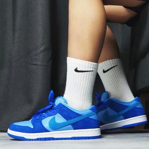 Blue Nike sneakers with white crew socks, shown from the side as a person stands indoors on a light floor.