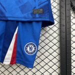 Close-up of a blue Chelsea FC jersey with crest, red and white stripe, against a chain-link fence.