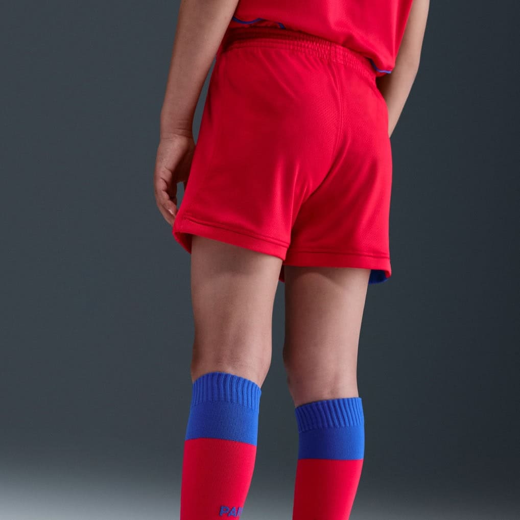 6t | UAE SPORT STORE Back view of a person in red athletic shorts and tall blue-and-red socks, standing on a dark background.