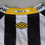 Close-up of a black-and-white checkered sports jersey collar with a yellow trim and an Umbro diamond logo in the center, plus a small SFC tag on the neck area.