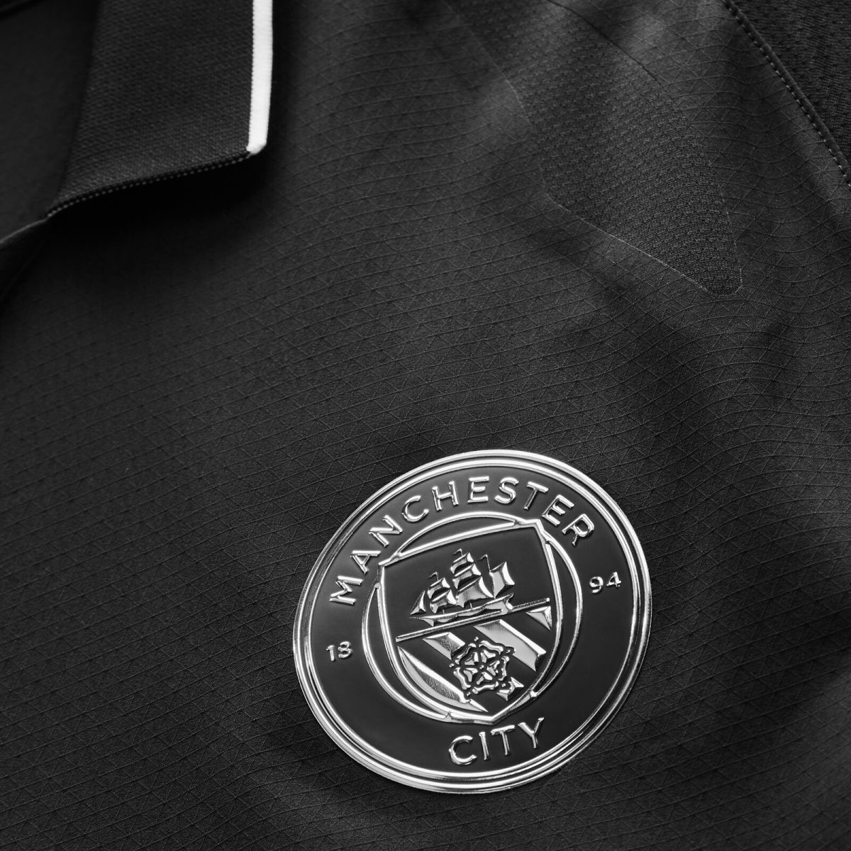 Close-up of a silver Manchester City crest badge on a black textured jacket.