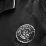 Close-up of a silver Manchester City crest badge on a black textured jacket.