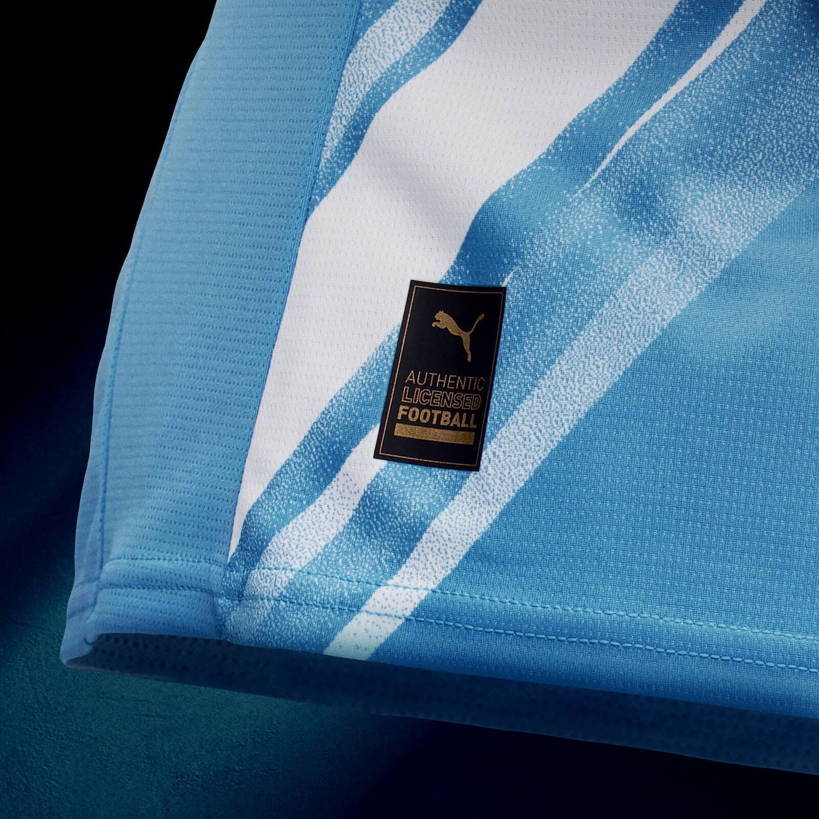 701237129001_pp_03_mcfc | UAE SPORT STORE Close-up of light blue striped football jersey fabric with a black Authentic Licensed Football tag.
