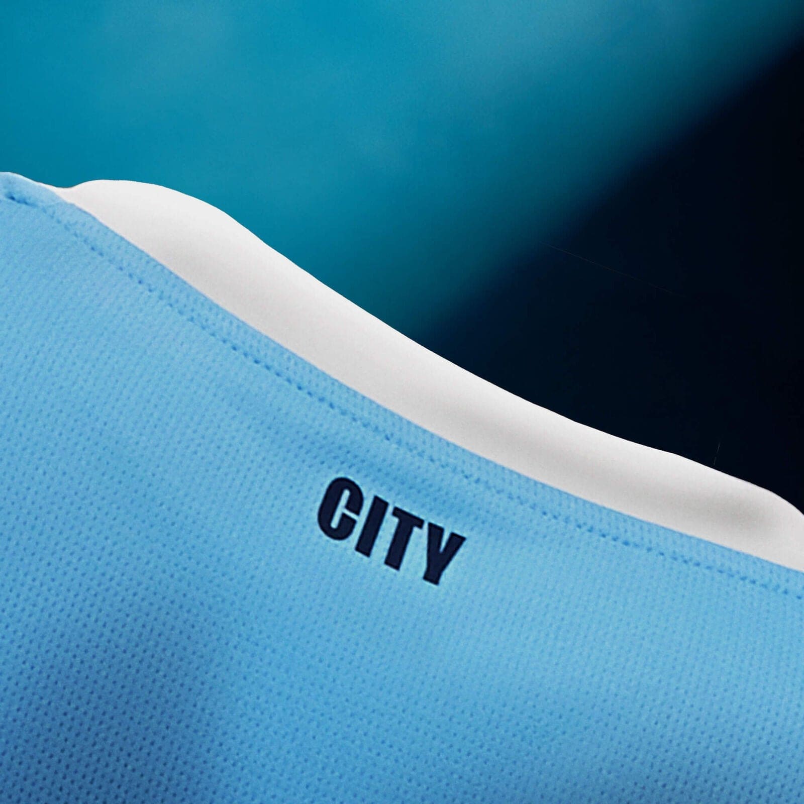 701237129001_pp_04_mcfc | UAE SPORT STORE Close-up of light blue perforated fabric with a white curved stripe and the word CITY printed in black.