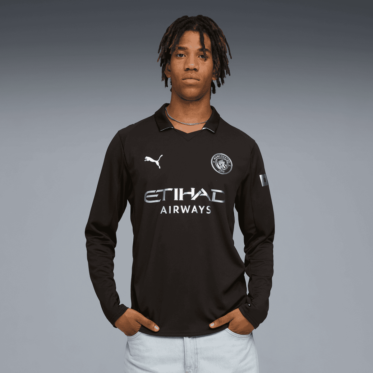 Young man in a black Manchester City jersey with Etihad Airways sponsor, standing against a gray gradient background.