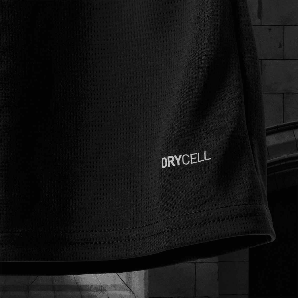 Close-up of black textured fabric with the word DRYCELL printed on it, showing a stitched seam at the bottom edge.