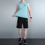 Man modeling a turquoise sleeveless athletic top with black Nike shorts and black sneakers.