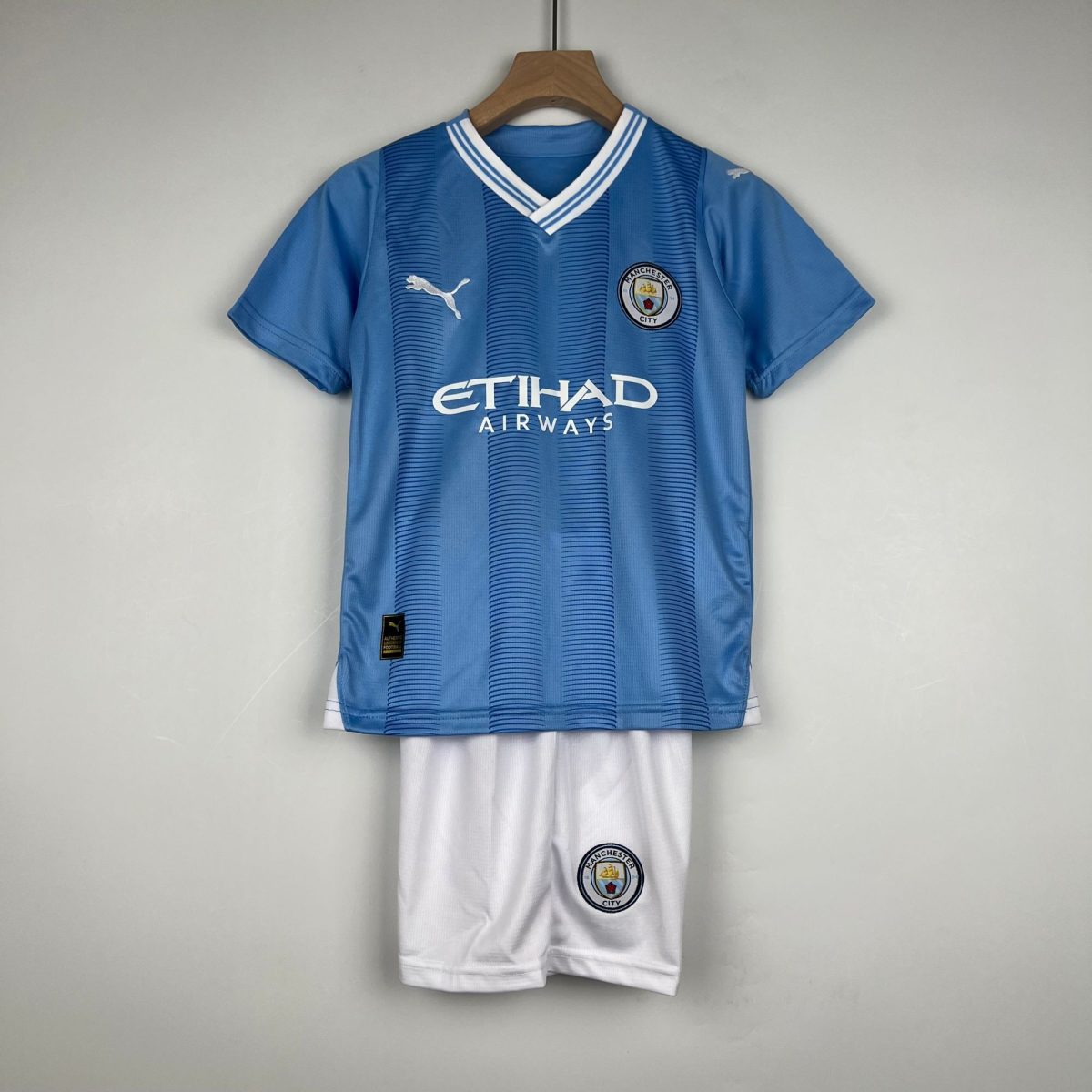 Blue Manchester City football jersey on a wooden hanger, with crest and Puma logo visible, paired with white shorts below