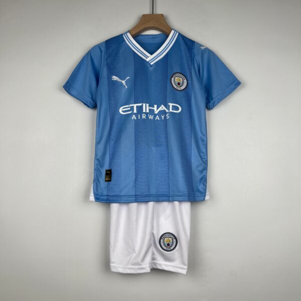 Blue Manchester City football jersey on a wooden hanger, with crest and Puma logo visible, paired with white shorts below