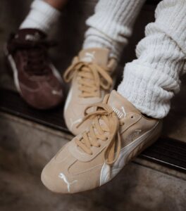 Beige Puma sneakers with white accents and laces, worn with chunky white socks, resting on a wooden step.