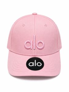 Pink baseball cap with pink embroidered 'alo' logo on the front and a black 'alo' sticker on the brim.