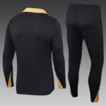 Black athletic tracksuit: long-sleeve top with tan collar and cuffs, paired with black pants featuring tan panels at the ankles.