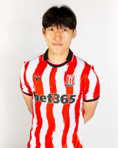 Young man in a Stoke City red-and-white striped football jersey posing against a white background, facing the camera.
