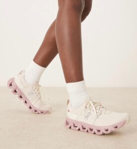 725249a6-c374-49a8-818a-8c4a04cf681f | UAE SPORT STORE Close-up of legs in white sneakers with pink chunky soles and white socks while walking on a light floor.