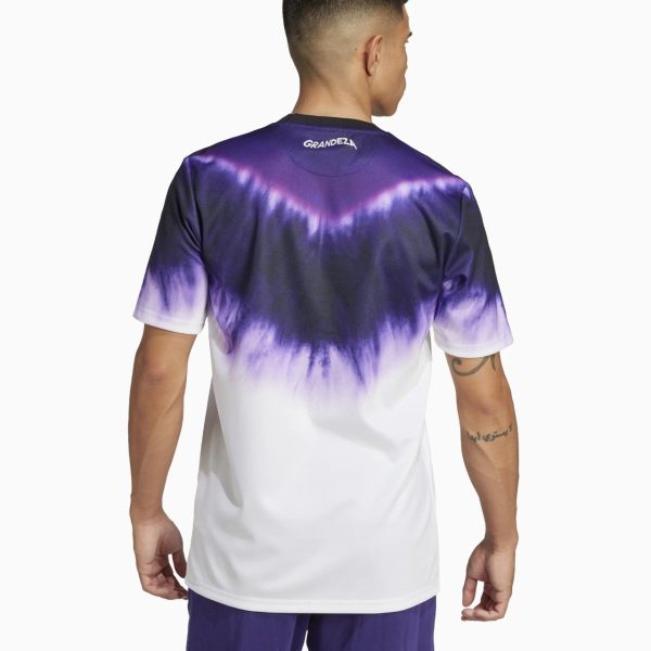 Back view of a man wearing a purple-to-white tie-dye T-shirt with a 'GRANDEZA' logo at the neckline and a visible forearm tattoo on the right arm.