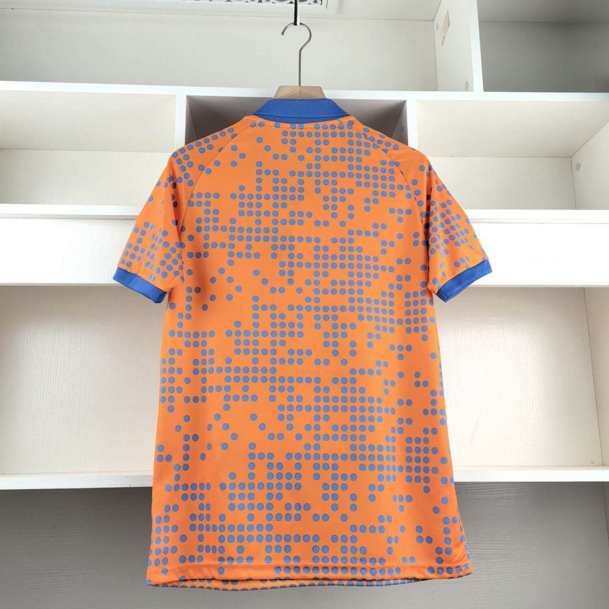 Orange short-sleeve shirt with a blue dotted pattern on a hanger in a closet, blue collar and sleeve cuffs visible.