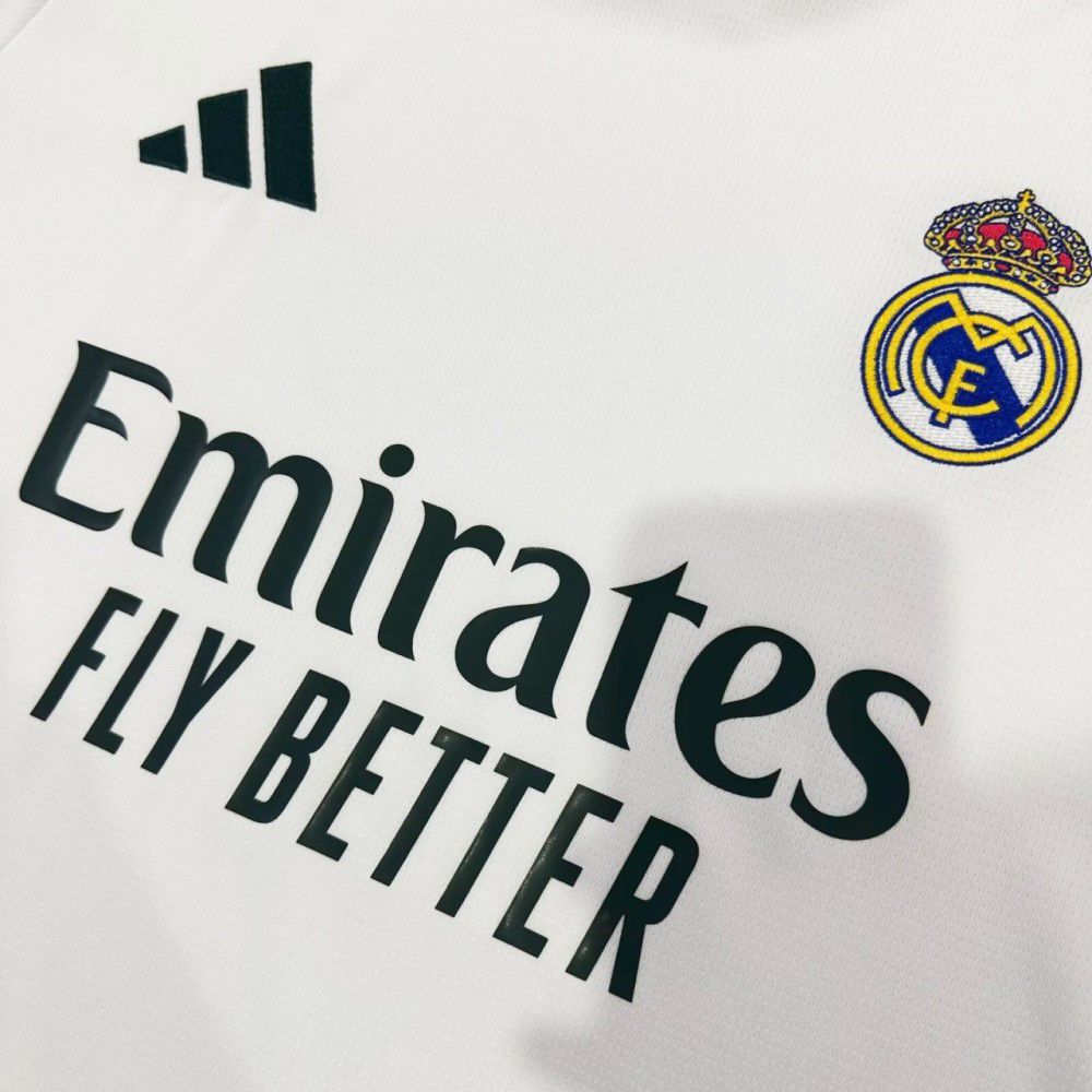 72d50d04-092d-4216-82d2-cef66e6a5b07 | UAE SPORT STORE Close-up of a white Real Madrid football jersey showing the Emirates Fly Better sponsor text and club crest on the right shoulder area.
