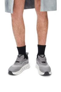Lower legs and feet wearing gray athletic sneakers with black socks, standing against a white background.