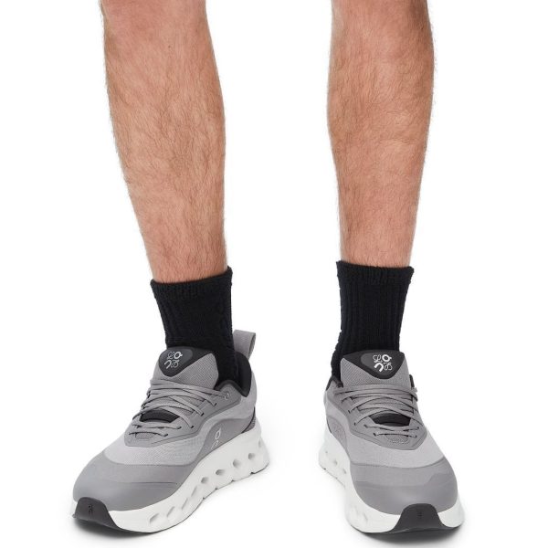 Lower legs and feet wearing gray athletic sneakers with black socks, standing against a white background.