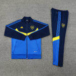 7323c9a8 | UAE SPORT STORE Blue and yellow tracksuit laid flat: zip-up jacket with navy sleeves, royal blue body, yellow chevron and CABJ crest, plus matching royal blue pants with three blue stripes and a yellow accent.