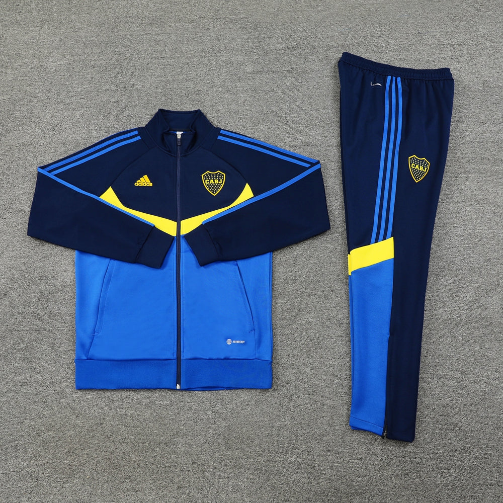 7323c9a8 | UAE SPORT STORE Blue and yellow tracksuit laid flat: zip-up jacket with navy sleeves, royal blue body, yellow chevron and CABJ crest, plus matching royal blue pants with three blue stripes and a yellow accent.