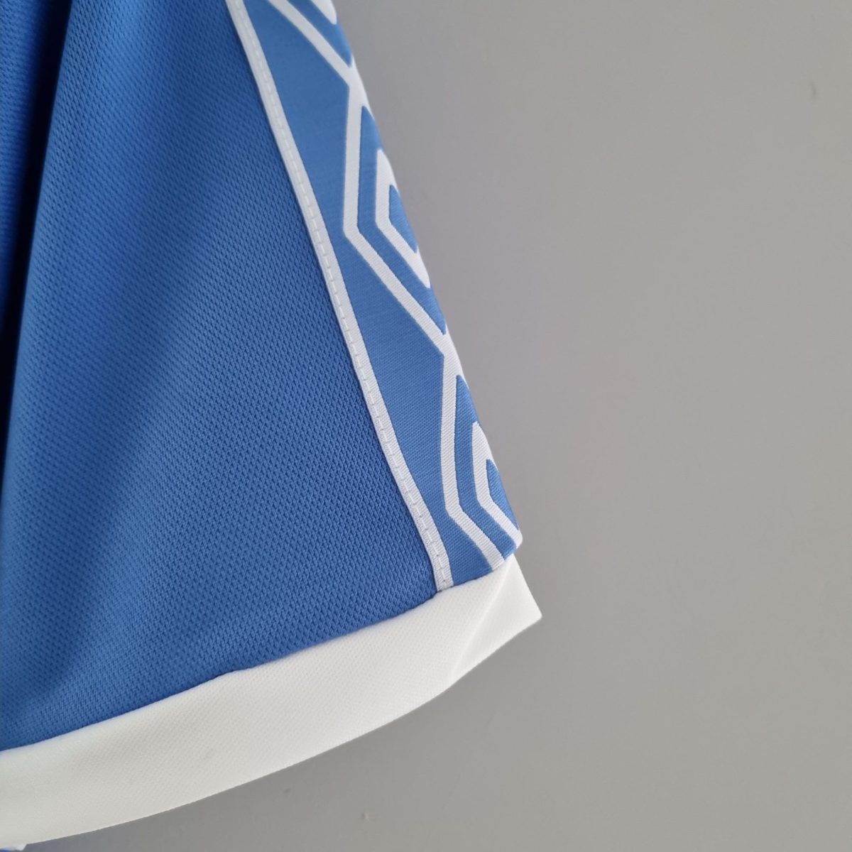 Close-up of blue textured fabric (mesh) with white stitched edge and white stripes, resembling a sports jersey detail.