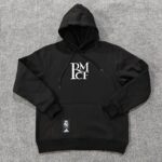 73d0cb5c | UAE SPORT STORE Black hoodie with hood up, white RM graphic on chest, laid on gray carpet; Real Madrid and Adidas tags attached.