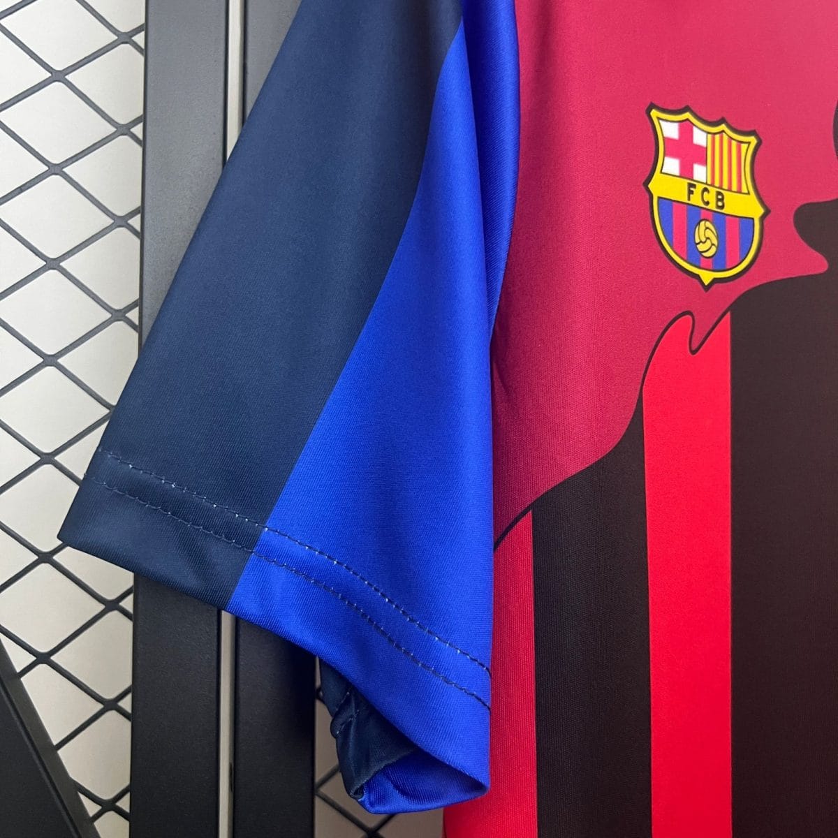 Close-up of blue and red Barcelona jerseys, with the club crest visible on the red fabric, against a gray tiled floor surface.
