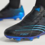73e1a524-c8dd-473c-8e0f-e5b1f64f2549 | UAE SPORT STORE Close-up of a black soccer boot with blue accents and blue studs on the sole area