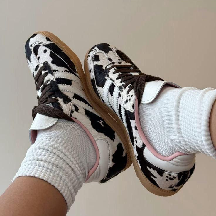 73f90309-2c5e-46bc-bb93-e893b0ac24a3 | UAE SPORT STORE Twin cow-print sneakers with white socks, laid back-to-back on a light background, highlighting a playful footwear look.