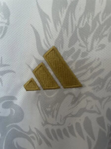 Gold embroidered three-triangle emblem on white patterned fabric (reminiscent of a mountain logo)
