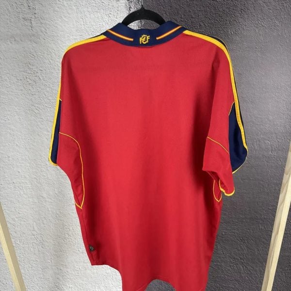 Back view of a red sports jersey with blue and yellow stripe details along the sleeves, hanging on a hanger.