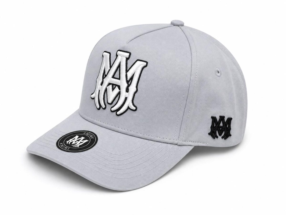 Light gray baseball cap with white-and-black embroidered M monogram on the front and a smaller black logo on the side, brim sticker visible on the brim.