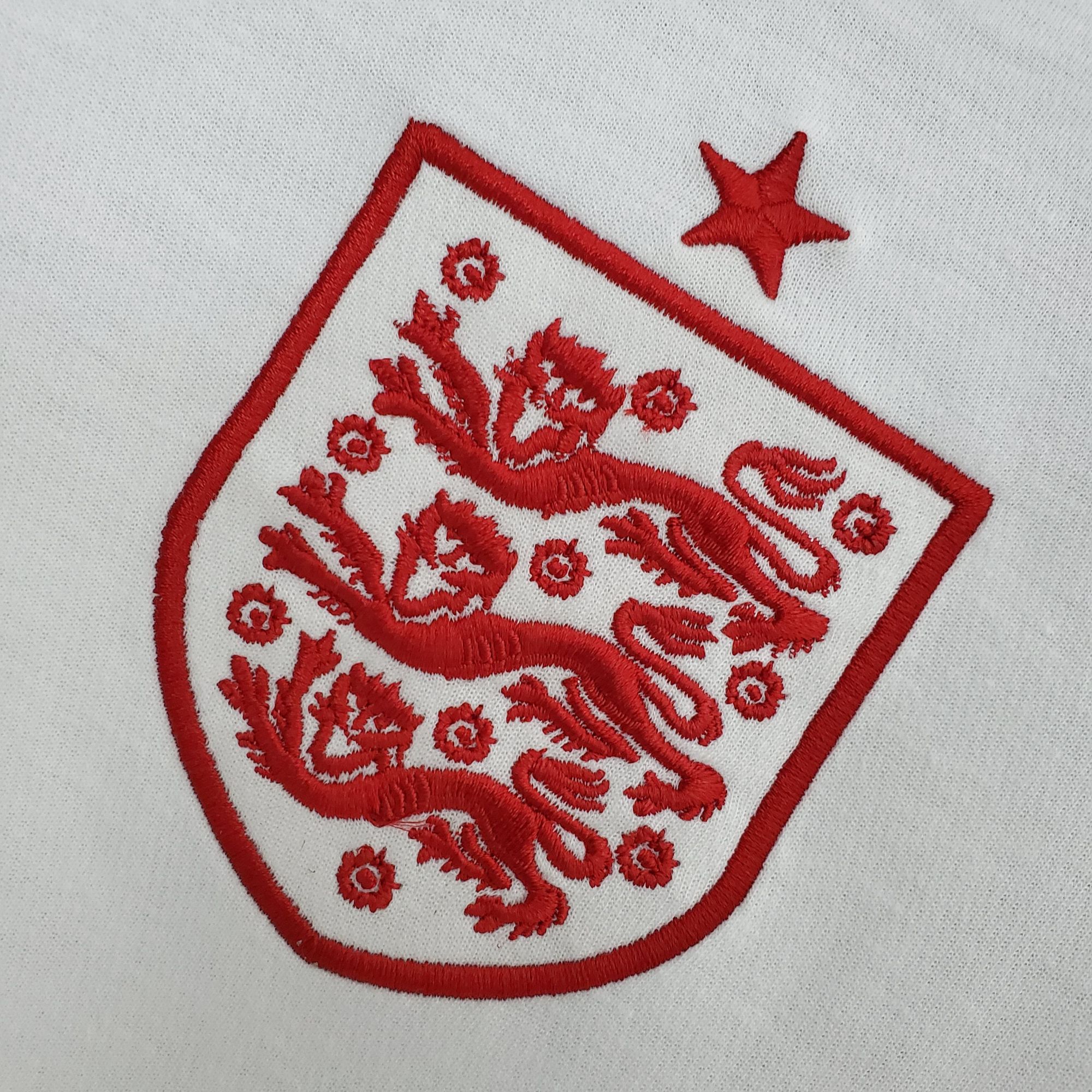 74a2614f_468deeca-8bd6-4b16-8889-6fabf89c3309 | UAE SPORT STORE Close-up of red embroidery on white fabric, showing a decorative border and floral motifs.