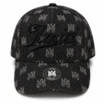 Black denim baseball cap with a repeated light logo pattern and a large embroidered cursive 'Amiri' on the front; round metal sticker on the brim.