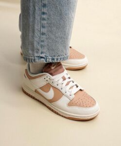Close-up of tan and white Nike sneakers with white laces, worn with light-wash jeans, on a pale floor.