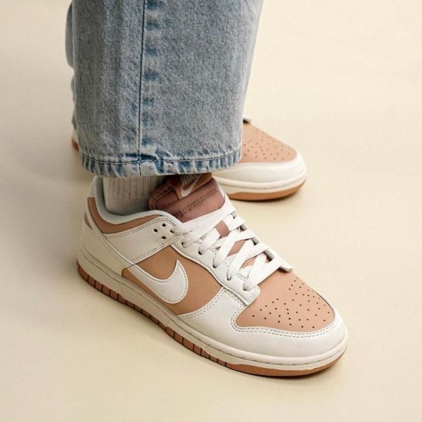 Close-up of tan and white Nike sneakers with white laces, worn with light-wash jeans, on a pale floor.