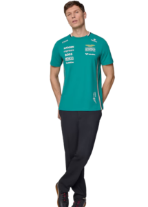 Man wearing a teal sports jersey with sponsor logos, dark pants, standing with one leg crossed in front on a white background