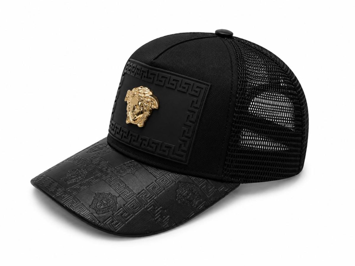 Black trucker cap with a decorative black panel and gold Medusa-style emblem on the front, and a patterned brim with a geometric design.