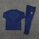 Navy blue athletic tracksuit laid flat on gray carpet: long-sleeve top and matching jogger pants, with a yellow crest on the pant leg.